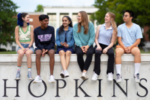 Six Summer at Hopkins Students sitting on the Hopkins sign at Homewood campus.