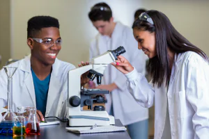 Three summer students, one about to look through a microscope.