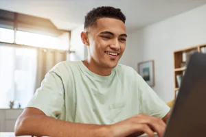 Summer student smiling, working on a laptop from home.
