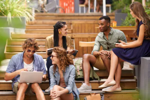 A group of summer students talking, looking at a laptop, sitting in a classroom.